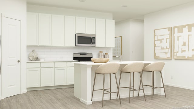 kitchen featuring white cabinetry, an island with sink, decorative backsplash, range, and light hardwood / wood-style flooring