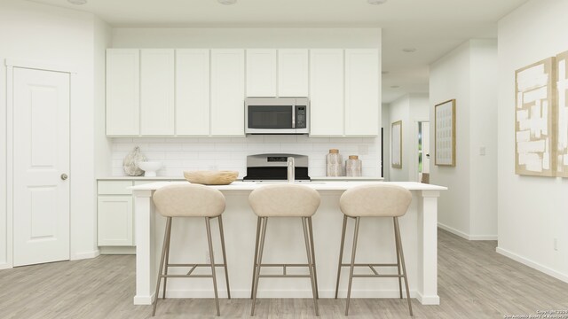 kitchen featuring stove, decorative backsplash, white cabinetry, and a center island with sink