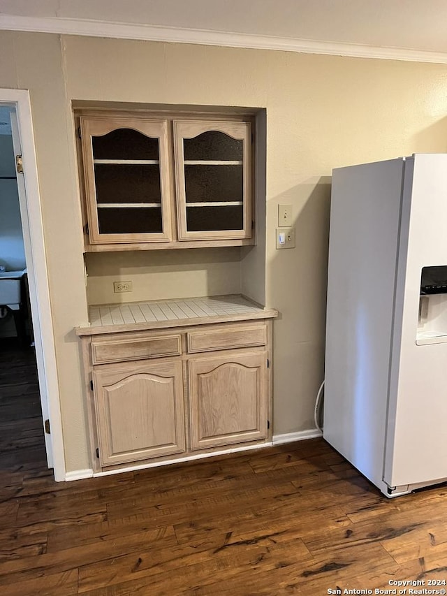 kitchen featuring tile counters, white refrigerator with ice dispenser, dark hardwood / wood-style flooring, and ornamental molding