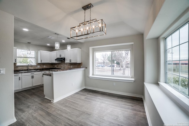 kitchen with kitchen peninsula, backsplash, white cabinets, and decorative light fixtures