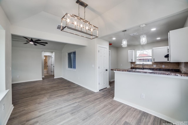 kitchen with ceiling fan with notable chandelier, pendant lighting, white cabinets, hardwood / wood-style floors, and backsplash