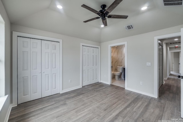 unfurnished bedroom with ceiling fan, lofted ceiling, two closets, light hardwood / wood-style flooring, and connected bathroom