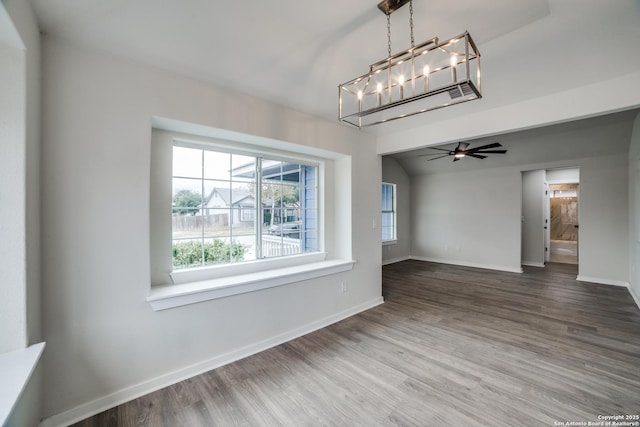 unfurnished dining area featuring ceiling fan with notable chandelier, hardwood / wood-style flooring, and vaulted ceiling