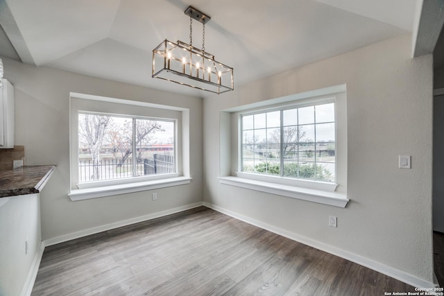 unfurnished dining area with vaulted ceiling, a chandelier, and hardwood / wood-style flooring