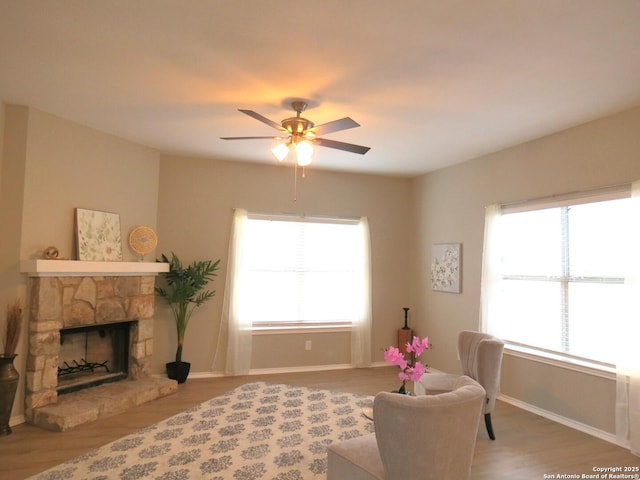 living area with ceiling fan, hardwood / wood-style floors, and a stone fireplace