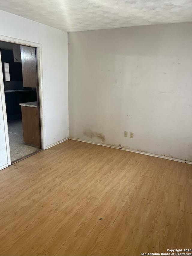 empty room with light wood-type flooring and a textured ceiling