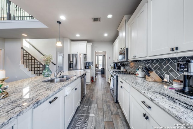 kitchen with sink, stainless steel appliances, light stone countertops, white cabinets, and decorative light fixtures