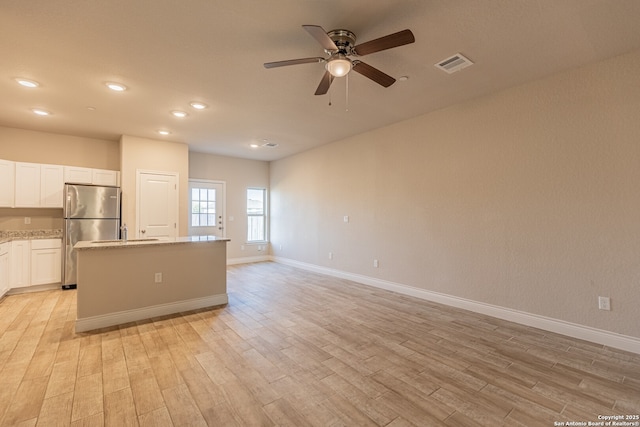 kitchen featuring light stone countertops, white cabinets, light hardwood / wood-style flooring, and stainless steel refrigerator