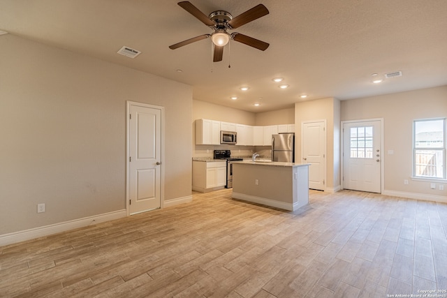 kitchen with light hardwood / wood-style floors, white cabinets, stainless steel appliances, and a kitchen island with sink