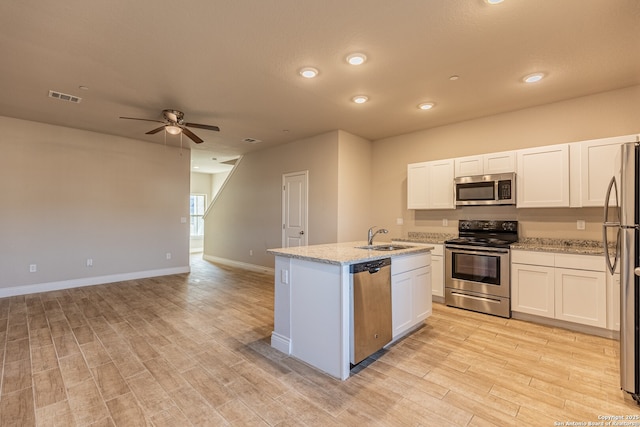 kitchen featuring appliances with stainless steel finishes, white cabinets, light stone counters, and a kitchen island with sink