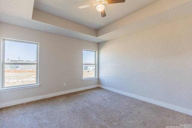 carpeted empty room with ceiling fan and a tray ceiling