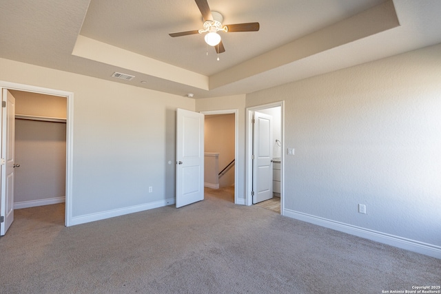 unfurnished bedroom featuring a walk in closet, a closet, ceiling fan, light colored carpet, and a tray ceiling