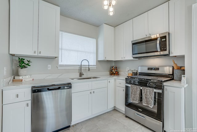 kitchen with appliances with stainless steel finishes, white cabinetry, sink, light tile patterned flooring, and light stone counters