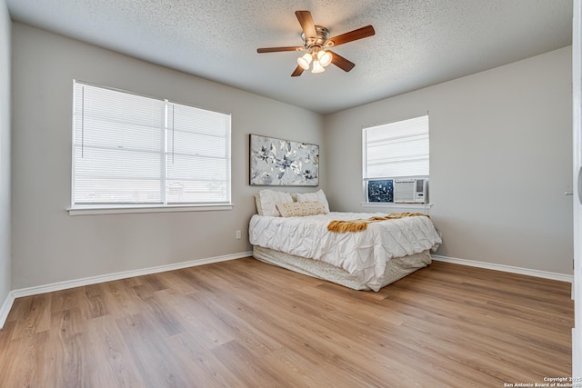 bedroom with ceiling fan, light hardwood / wood-style floors, multiple windows, and a textured ceiling