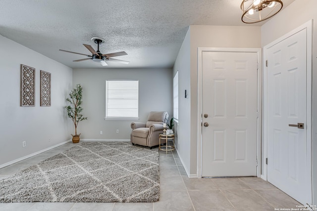 foyer entrance with ceiling fan with notable chandelier, a textured ceiling, and light tile patterned floors