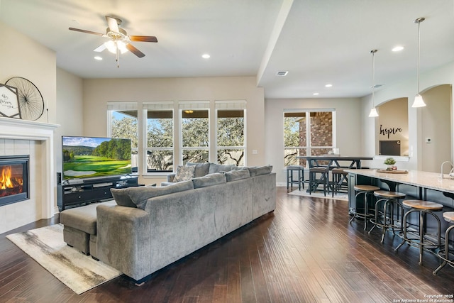 living room with ceiling fan, dark wood-type flooring, and a tile fireplace