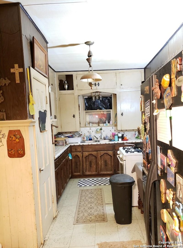 kitchen featuring fridge, sink, white gas range, and dark brown cabinets