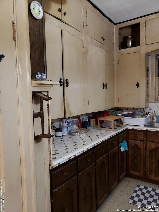 kitchen featuring light tile patterned floors, tile counters, decorative backsplash, and dark brown cabinetry