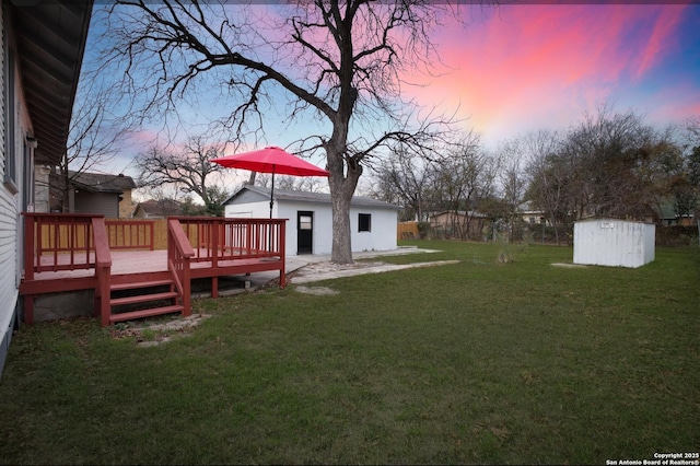 yard at dusk featuring a storage unit and a deck