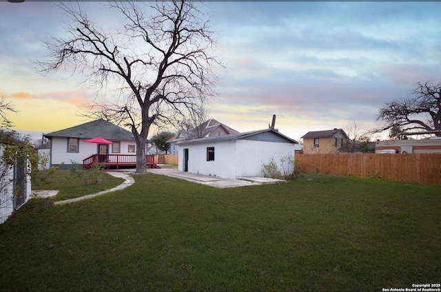 yard at dusk with a wooden deck and a patio