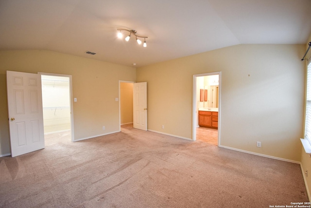 unfurnished bedroom featuring ensuite bathroom, light carpet, and vaulted ceiling