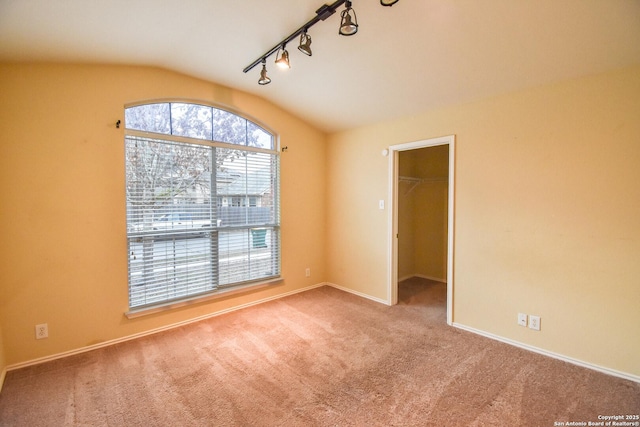 empty room featuring vaulted ceiling, rail lighting, and light colored carpet