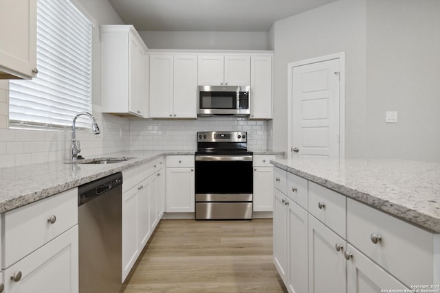 kitchen with light stone countertops, appliances with stainless steel finishes, white cabinetry, and sink