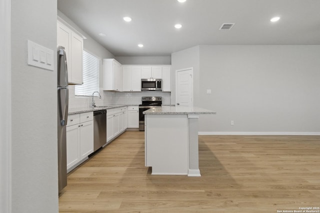 kitchen featuring stainless steel appliances, light wood-type flooring, a kitchen island, white cabinets, and light stone counters