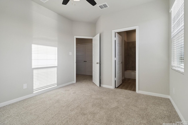 unfurnished bedroom with light carpet, a spacious closet, ensuite bathroom, ceiling fan, and a closet