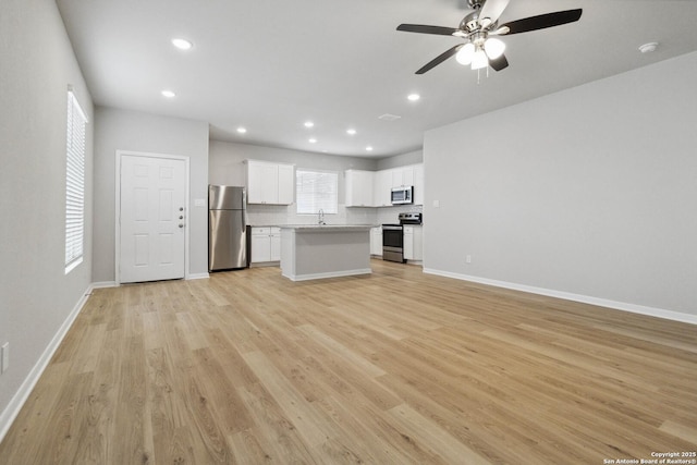 unfurnished living room featuring ceiling fan, sink, and light wood-type flooring