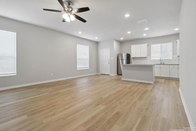 unfurnished living room with ceiling fan, light wood-type flooring, and sink