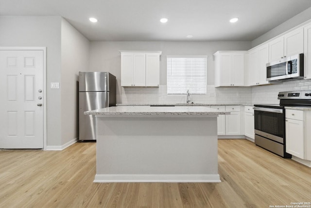 kitchen with stainless steel appliances, light hardwood / wood-style floors, white cabinetry, and a center island