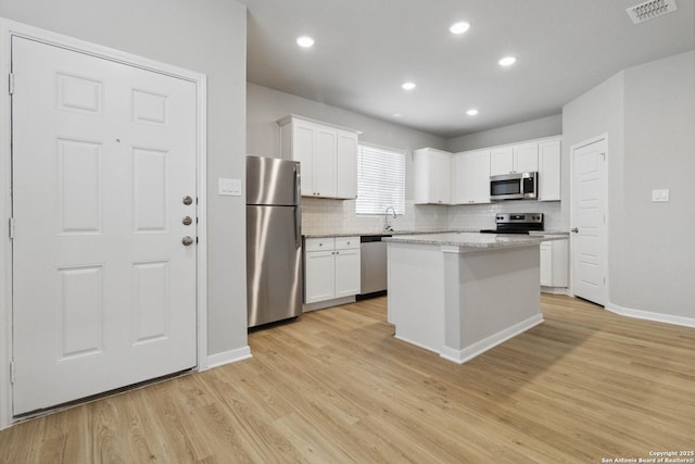 kitchen with light stone counters, stainless steel appliances, white cabinets, and a kitchen island