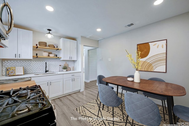 kitchen with white cabinets, tasteful backsplash, sink, black gas stove, and light hardwood / wood-style flooring