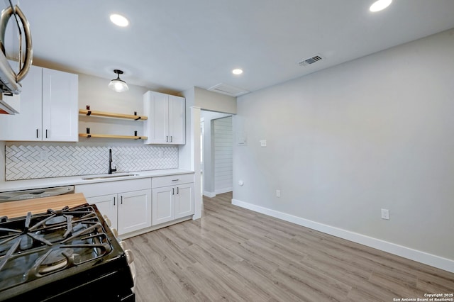 kitchen featuring gas stove, backsplash, white cabinets, and sink