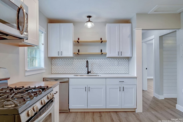 kitchen with appliances with stainless steel finishes, sink, white cabinetry, and pendant lighting