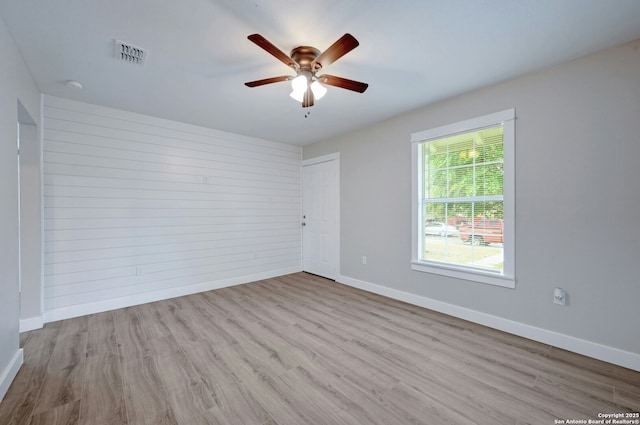 spare room with light wood-type flooring, ceiling fan, and wood walls