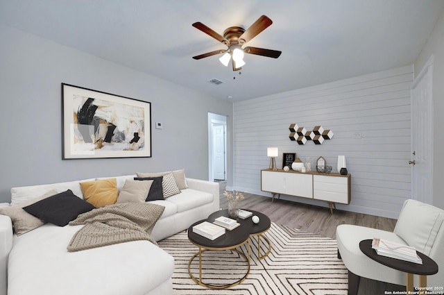 living room featuring ceiling fan, light wood-type flooring, and wooden walls