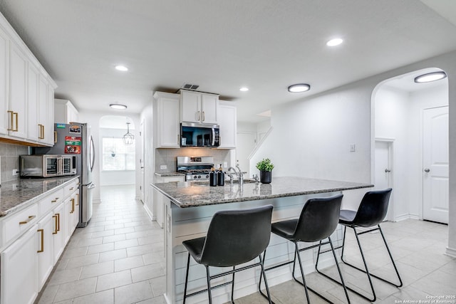 kitchen with white cabinets, stainless steel appliances, decorative backsplash, a kitchen island with sink, and light tile patterned floors