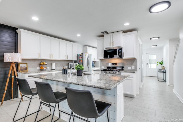 kitchen with an island with sink, a breakfast bar area, appliances with stainless steel finishes, white cabinets, and light stone counters