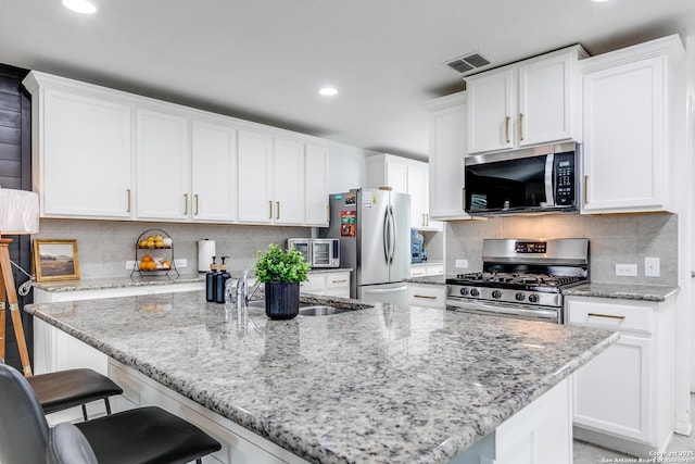 kitchen with white cabinets, a breakfast bar, light stone counters, and stainless steel appliances