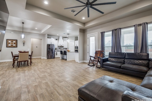 living room featuring a raised ceiling, ceiling fan, and light hardwood / wood-style floors