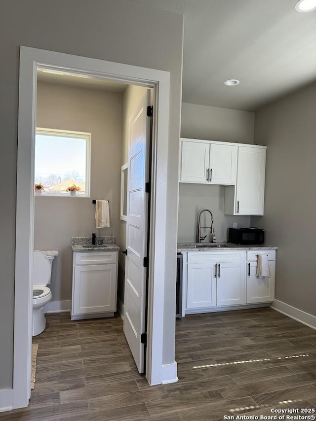 kitchen featuring light stone counters, sink, and white cabinetry