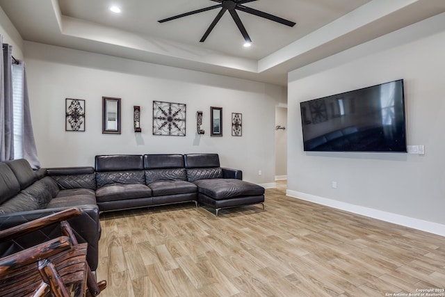 living room featuring a raised ceiling, ceiling fan, and light hardwood / wood-style flooring