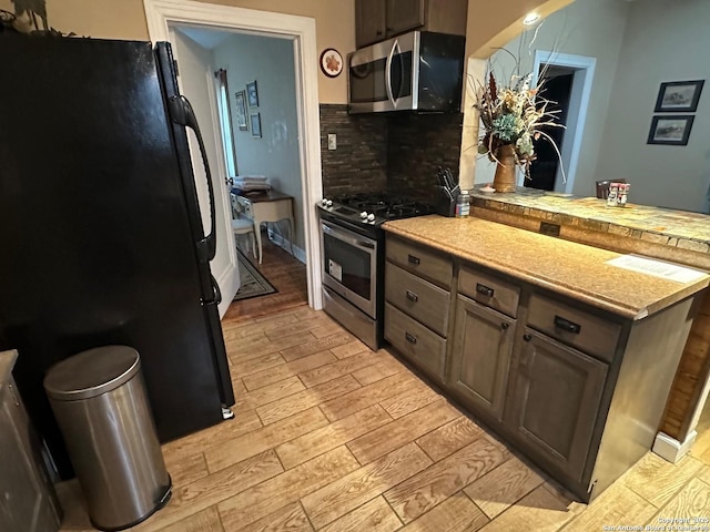 kitchen with light hardwood / wood-style floors, kitchen peninsula, appliances with stainless steel finishes, tasteful backsplash, and dark brown cabinets