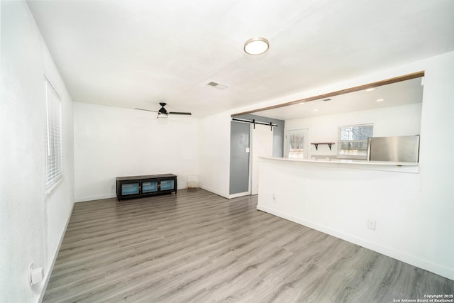 unfurnished living room featuring ceiling fan, a barn door, and hardwood / wood-style floors