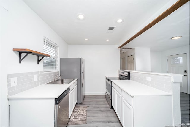 kitchen with appliances with stainless steel finishes, white cabinetry, tasteful backsplash, kitchen peninsula, and light wood-type flooring