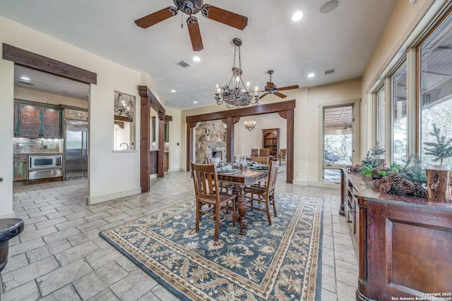 dining space featuring ceiling fan with notable chandelier and a stone fireplace