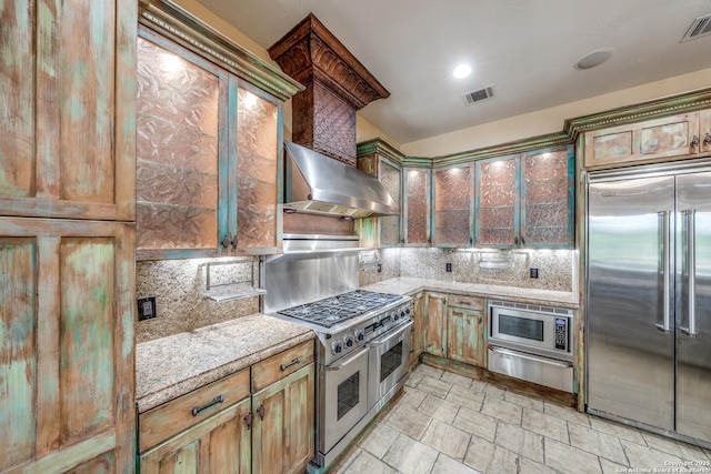 kitchen with backsplash, wall chimney exhaust hood, and built in appliances