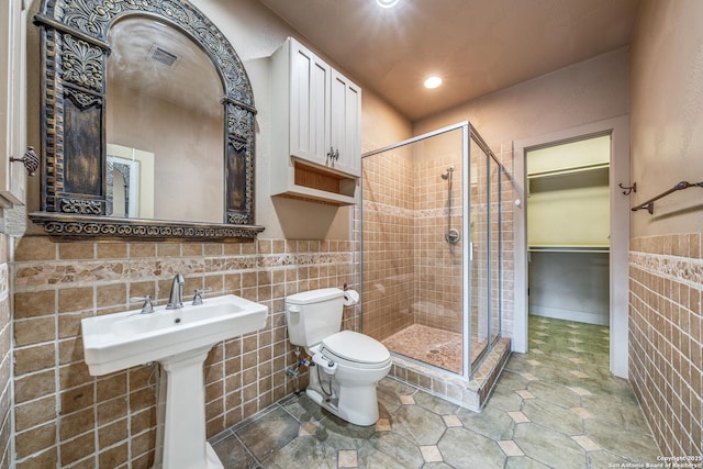 bathroom with an enclosed shower, sink, tile walls, and toilet